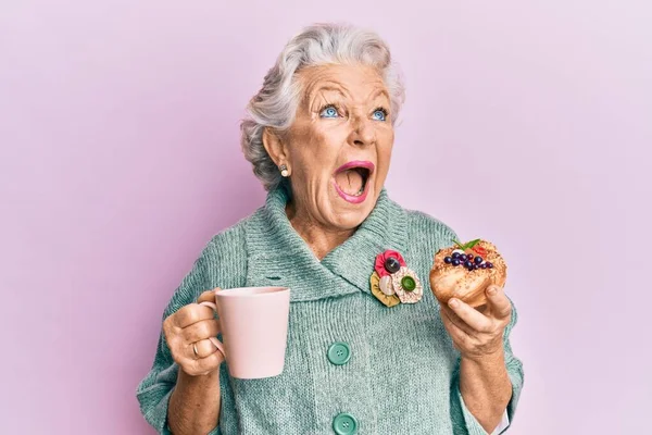 Starsza Siwowłosa Kobieta Pije Filiżankę Kawy Bułki Wściekła Wściekła Krzycząc — Zdjęcie stockowe