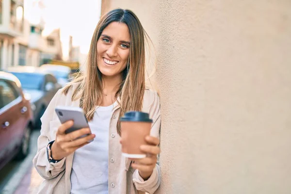 Νεαρή Καυκάσια Γυναίκα Χαμογελώντας Ευτυχισμένη Χρησιμοποιώντας Smartphone Και Πίνοντας Παίρνει — Φωτογραφία Αρχείου