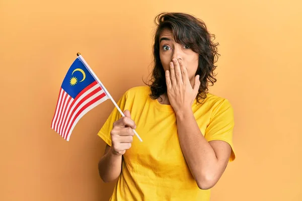 手で口をカバーするマレーシアのフラグを保持若いヒスパニック系の女性 ショックを受け ミスを恐れて 驚きの表情 — ストック写真