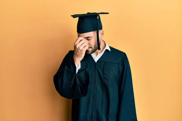 卒業キャップと儀式用のローブを身に着けている若いヒスパニック系の男は 鼻や目をこすり疲れて疲労や頭痛を感じます ストレスとフラストレーションの概念 — ストック写真