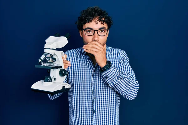 Young Hispanic Man Holding Microscope Covering Mouth Hand Shocked Afraid — Stock Photo, Image