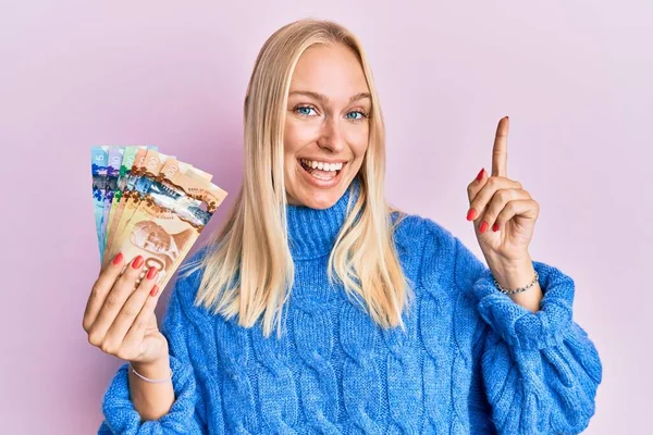 Młoda Blondynka Trzyma Kanadyjskie Dolary Uśmiechając Się Zdumiony Zaskoczony Wskazując — Zdjęcie stockowe
