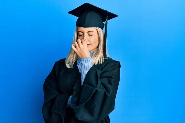 卒業キャップと式のローブを着た美しいブロンドの女性は 臭いと嫌な 耐えられない匂いを嗅ぎ 鼻の上に指で息を保持します 臭いが悪い — ストック写真