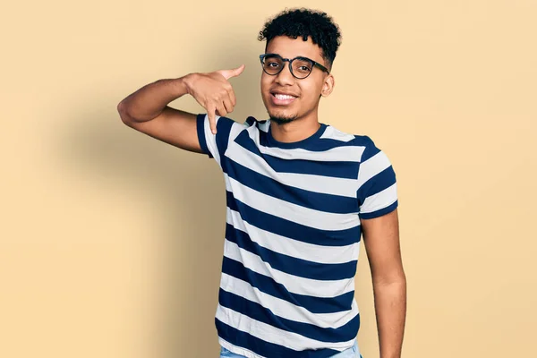 年轻的非洲裔美国人 身穿休闲装 戴着眼镜 微笑着 用手和手指做着电话手势 就像在电话里说话一样 交流概念 — 图库照片