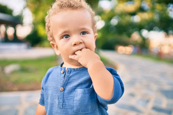 在阳光灿烂的日子里 公园里的牙疼 让可怜的小男孩用手指捂住嘴 摸着牙龈 漂亮的金发碧眼的男婴在户外痛苦地寻找新的婴儿牙 — 图库照片