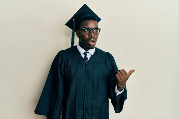 Handsome Black Man Wearing Graduation Cap Ceremony Robe Surprised Pointing — Stock Photo, Image