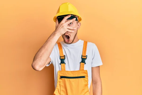 Joven Hispano Vistiendo Uniforme Constructor Casco Seguridad Asomándose Shock Cubriendo — Foto de Stock