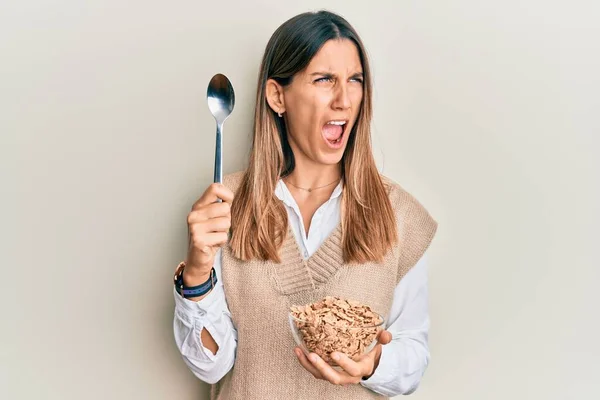 ブルネットの若い女性は怒っているスプーンで健康的な全粒穀物を食べると怒りを叫び フラストレーションと激怒 怒って叫んでいる 怒りと攻撃的な考え方 — ストック写真