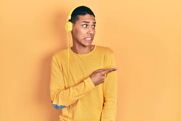 一个年轻的非洲裔美国人 用耳机听音乐 用食指 关心和惊讶的表情将焦虑和紧张抛在一边 — 图库照片