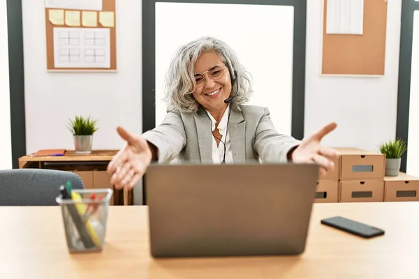 中年女商人坐在办公桌前工作 在办公室里用笔记本电脑看着摄像机 张开双臂拥抱对方 欢快的表达拥抱幸福 — 图库照片