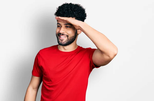 年轻的阿拉伯男子 留着胡子 穿着休闲的红色T恤 非常高兴 面带微笑地看着远方 手牵着手 搜索概念 — 图库照片