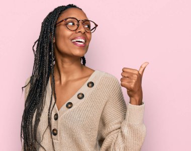 Afro-Amerikan kadın, günlük kıyafetler giyip gülümsüyor, gülümsüyor ve başparmağıyla yan tarafa bakıyor.. 