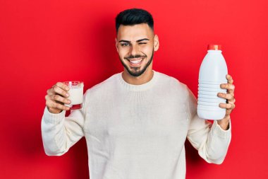 Sakallı, elinde bir bardak süt ve plastik şişe olan genç İspanyol adam kameraya seksi bir ifadeyle bakıyor, neşeli ve mutlu bir yüzle.. 