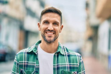 Genç beyaz adam gülümseyerek şehirde mutlu mesut duruyor..