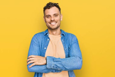 Gündelik kıyafetler giyen, kollarını kavuşturup kameraya gülümseyen genç İspanyol adam. pozitif kişi. 