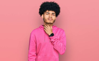 Afro saçlı, sıradan pembe kazaklı, boynu ağrıyan, grip, mantar ve enfeksiyon yüzünden boğaz ağrıyan Afro-Amerikan genç adam. 