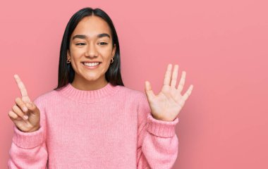 Genç Asyalı kadın, günlük kışlık süveter giyer ve altı numaralı parmaklarıyla gülümseyerek mutlu ve kendinden emin bir şekilde onu işaret eder.. 