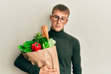 Kafkasyalı genç bir adam elinde torbayla market alışverişi yaparken düşünceli ve ayık bir ifade takınıyor. Kendinden emin görünüyor. 