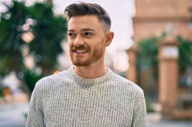 Genç beyaz adam gülümseyerek şehirde mutlu mesut duruyor..