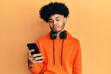Afro saçlı Afro-Amerikan genç adam akıllı telefon kullanıyor. Depresyonda ve sıkıntıdan endişe ediyor. Kızgın ve korkmuş. hüzünlü ifade. 