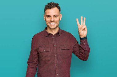 Gündelik kıyafetler giyen genç İspanyol adam üç numarayı gösterip işaret ederken kendinden emin ve mutlu gülümsüyor.. 