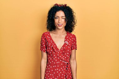 Yazlık elbise giyen genç Latin kız kameraya seksi bir ifadeyle bakıyor, neşeli ve mutlu bir yüzle.. 