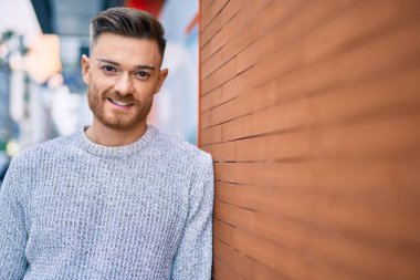 Genç beyaz adam gülümseyerek şehirde mutlu mesut duruyor..