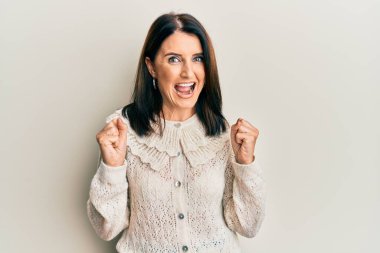 Orta yaşlı esmer kadın gündelik giysiler giyip kollarını kaldırarak ve açık gözlerle başarıyı kutluyor. Kazanan konsept. 