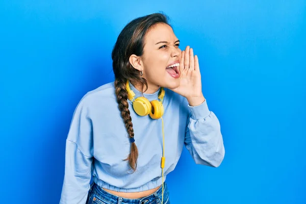 若いヒスパニック系の女の子は ヘッドフォンの叫びを使用して音楽を聞いて 口の上に手で横に大声で叫ぶ コミュニケーションの概念 — ストック写真