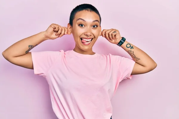 短い髪をした美しいヒスパニック系の女性は 指で耳を引く笑みを浮かべてカジュアルなピンクのTシャツを着て 面白いジェスチャー オーディション問題 — ストック写真