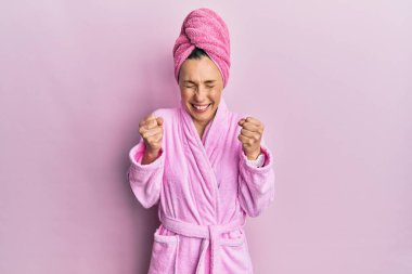 Duş havlusu şapkası ve bornoz giyen genç sarışın kadın başarı için heyecanlanıyor kolları havada ve gözleri kapalı zaferi kutluyor. Kazanan konsept. 