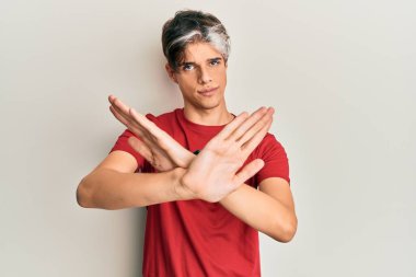 Gündelik kıyafetler giyen genç İspanyol adam. Reddedilmiş yüz ifadesi. Kollarını kavuşturup negatif işaret veriyor. 