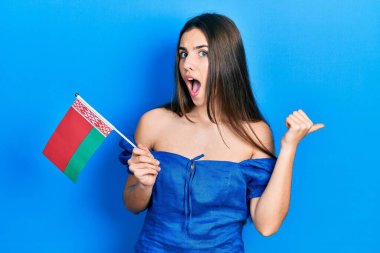 Genç esmer genç, Belarus bayrağını tutarken başparmağını kaldırıyor ve ağzı açık gülümsüyor. 