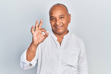 Orta yaşlı, sıradan kıyafetler giyen, gülümseyen ve el ve parmaklarıyla 