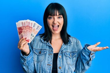 Genç İspanyol kadın elinde İzlanda Krona banknotları ile başarıyı mutlu bir gülümsemeyle kutluyor ve kazanan el kaldırarak ifade ediyor 