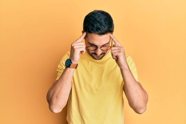 Baskı yüzünden başı ağrıyan gündelik kıyafetler ve gözlük takan genç İspanyol bir adam. migren ağrısı. 