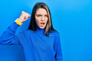 Balıkçı yaka kazak giyen genç esmer kız öfkeyle bağırırken kızgın ve kızgın bir şekilde yumruk kaldırıyor. öfke ve agresif konsept. 