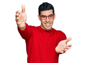 Yakışıklı İspanyol bir adam günlük kıyafetler ve gözlük takıyor kameraya bakıyor kucaklaşmak için kollarını açmış gülümsüyor. Mutluluğu kucaklayan neşeli bir ifade.. 