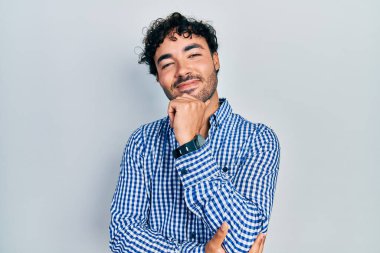 Gündelik kıyafetler giyen genç İspanyol adam kameraya bakıyor kollarını kavuşturup gülümseyerek ve çenesini kaldırarak. Olumlu düşünmek. 