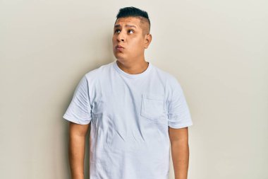 Gündelik beyaz tişört giyen genç latin adam gülümseyip yan tarafa bakıyor ve düşünüyor.. 