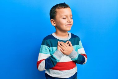 Çizgili süveter giyen, elleri göğsünde gülümseyen, gözleri kapalı, yüzünde minnet ifadesi olan küçük bir çocuk. sağlık kavramı. 