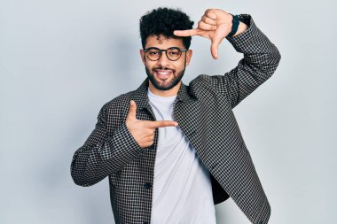 Sakallı, gözlüklü, gülümseyen, elleri ve parmakları gülen yüzlü genç bir Arap. yaratıcılık ve fotoğrafçılık kavramı. 