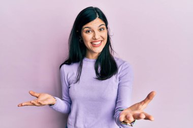 Genç İspanyol kadın gündelik giysiler giyiyor. Neşeli gülümsüyor, kollarını açıyor. Hoş geldin, olumlu ve kendinden emin selamlar. 