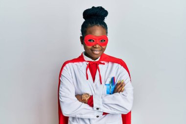 Genç Afro-Amerikan kadın doktor üniforması giyiyor ve süper kahraman kostümü giyip kollarını kavuşturup kameraya gülümsüyor. pozitif kişi. 