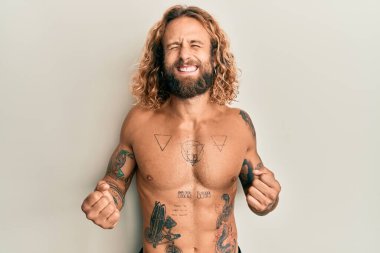 Sakallı, uzun saçlı, kolları havada ve gözleri kapalı zaferi gülümseyerek kutlayan başarılı dövmeleri olan yakışıklı bir adam. Kazanan konsept. 