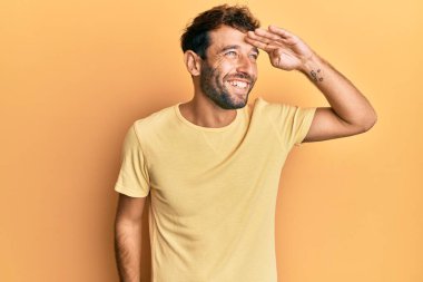 Sarı arka planda sıradan sarı tişörtler giyen sakallı yakışıklı bir adam. Çok mutlu ve tebessüm ediyor. arama kavramı. 