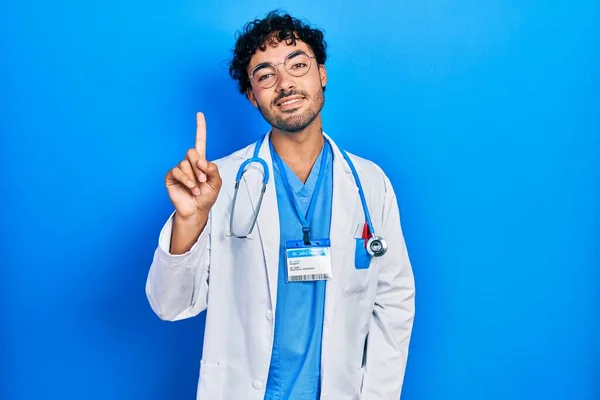 身穿医生制服 带着听诊器的年轻人面带微笑 面带微笑 手指头指向一边 — 图库照片