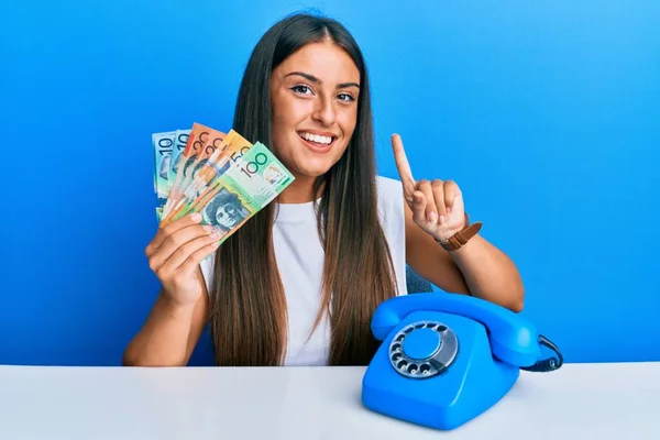Piękna Latynoska Kobieta Zabytkowym Telefonem Trzymająca Australijskie Dolary Uśmiechnięta Pomysłem — Zdjęcie stockowe