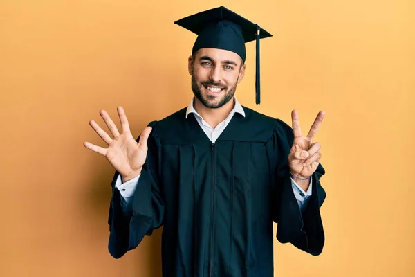 自信と幸せ笑顔ながら卒業キャップと式のローブを身に着けている若いヒスパニック男が現れ 指番号7で指摘します — ストック写真