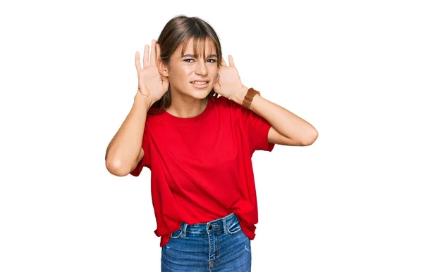 十代の白人の少女は 耳のジェスチャーで両方の手を聞くしようとしてカジュアルな赤いTシャツを着て ゴシップを好奇心 聴覚障害や聴覚障害 — ストック写真